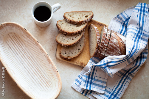 Sliced bread on a woody cutting board on desk with bascet, cup o