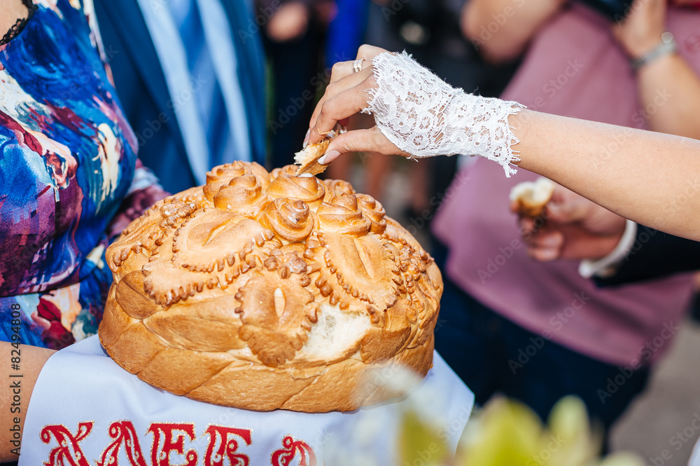 Groom holding slice of traditional wedding round loaf and bride