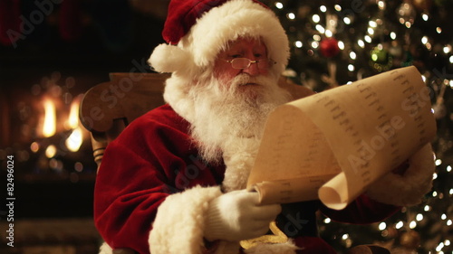 Santa Claus reading his naughty and nice list in a chair by the fire