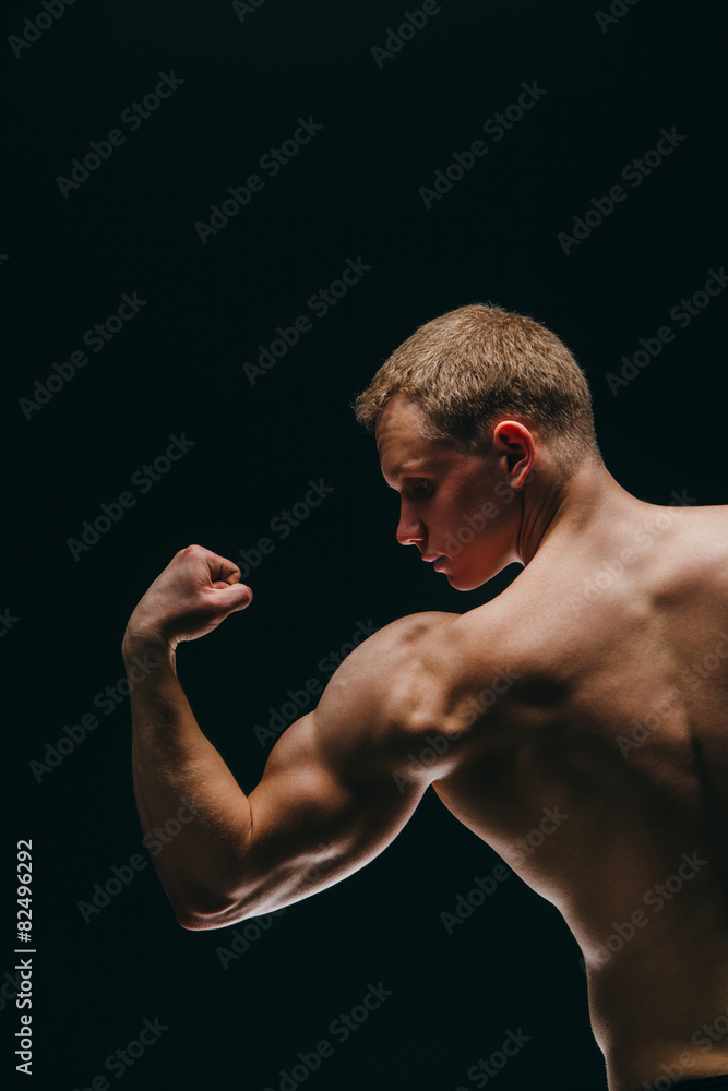 muscular young man showing his biceps isolated on black muscular young man showing his biceps isolated on black