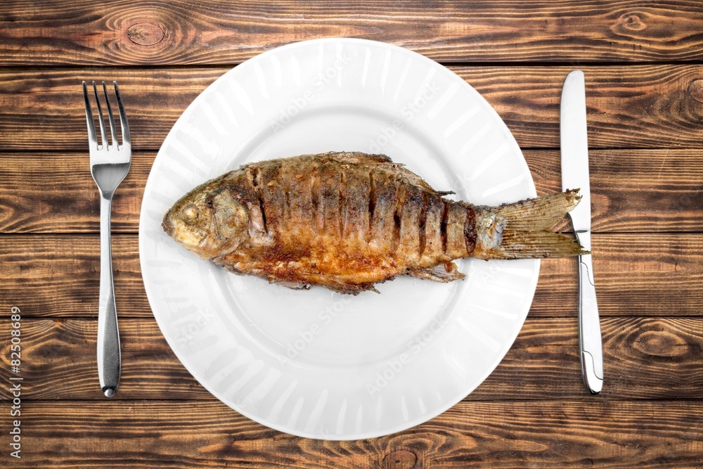 Fish. Fried fish on white plate with fork and knife, closeup