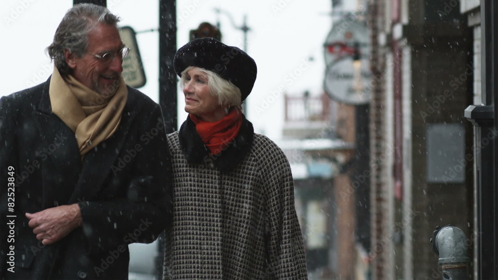senior couple walking down a snowy street and kissing senior couple walking down a snowy street and kissing