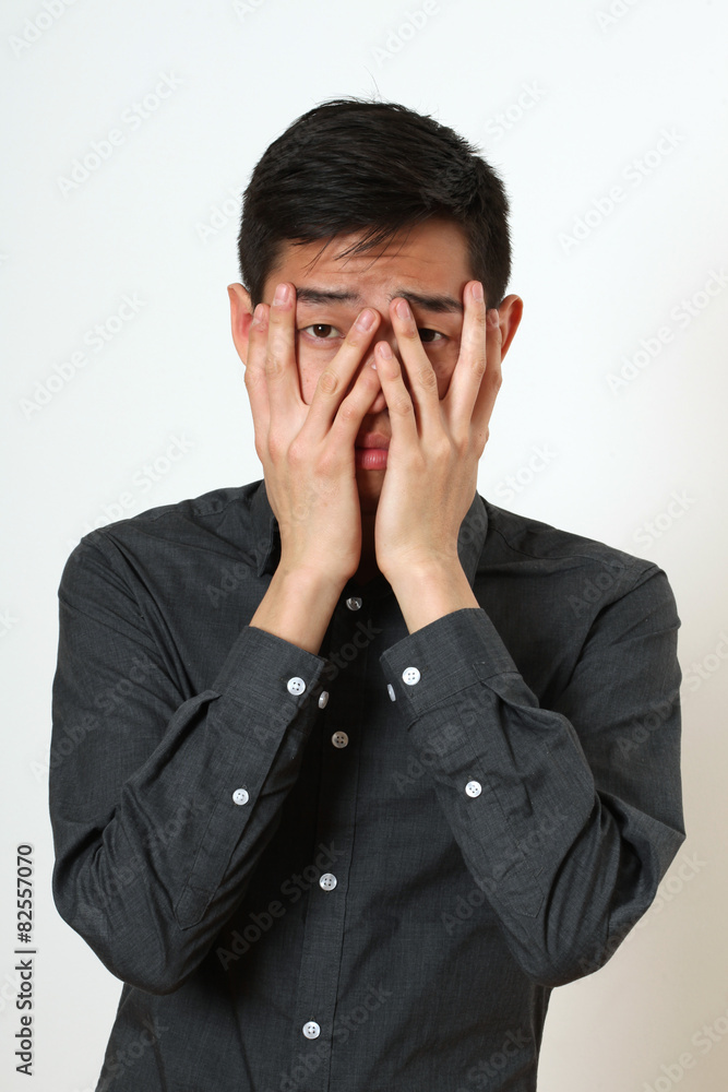Frustrated young Asian man covering his face with palms Frustrated young Asian man covering his face with palms