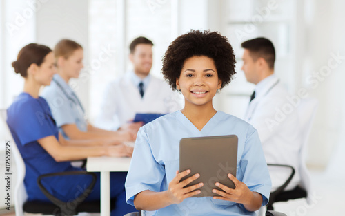 happy doctor with tablet pc over team at clinic