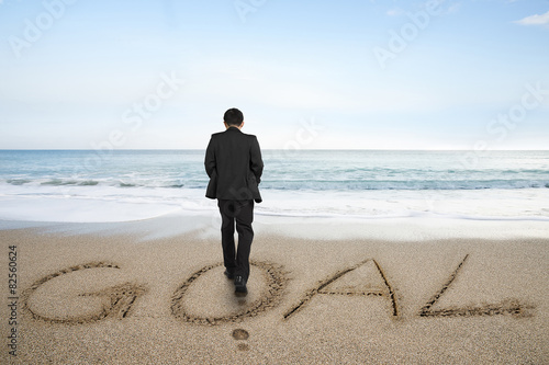 Rear view businessman standing with goal word on sand beach