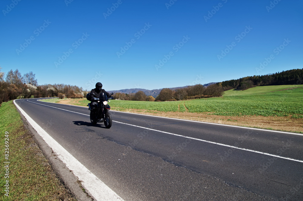 Black motorcycle traveling on the road in rural landscape