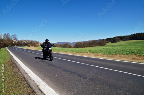 Black motorcycle traveling on the road in rural landscape © am