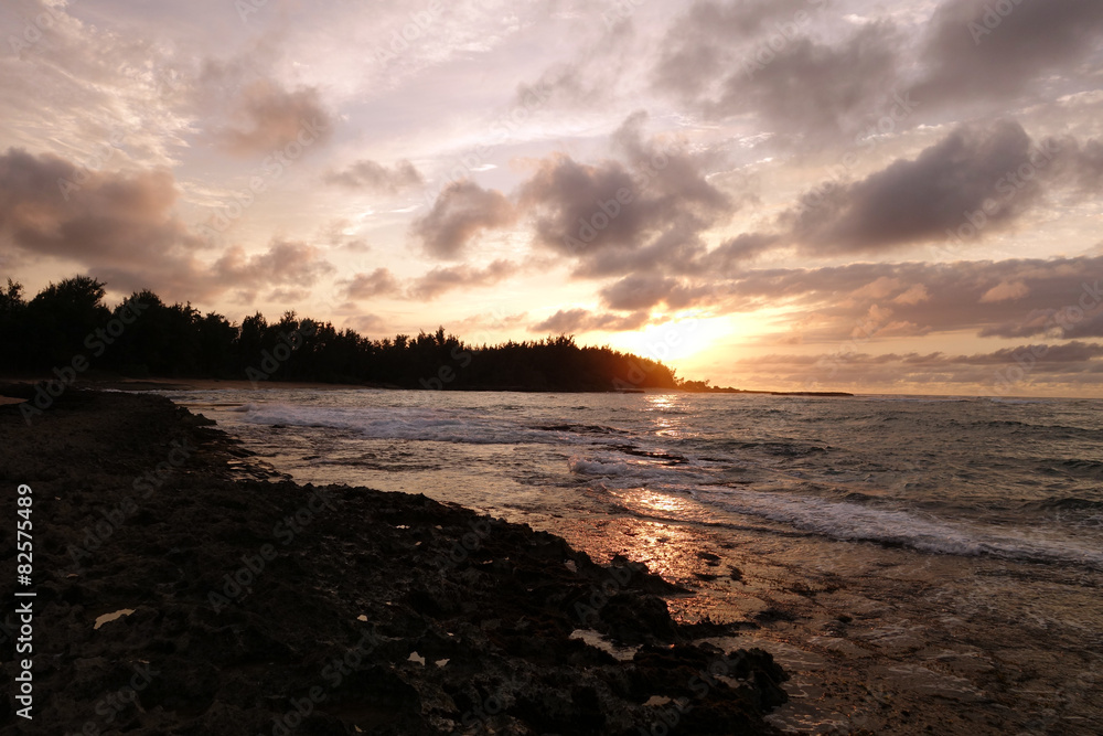 Fototapeta premium Sunset through the clouds and reflecting on the waves as they br