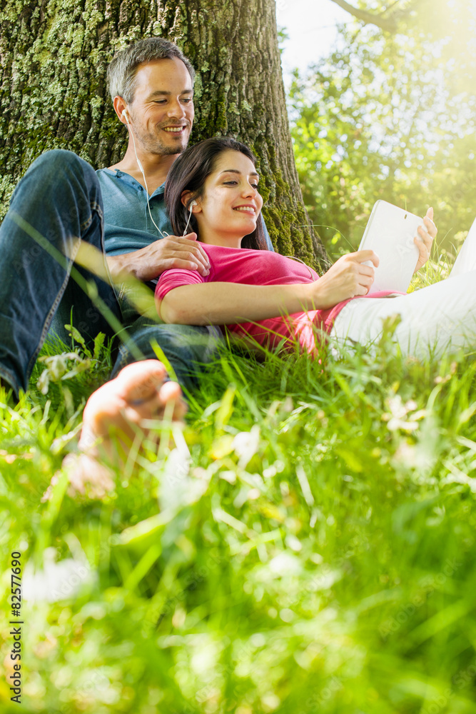 Fototapeta premium A nice couple sitting in the grass, using a tablet