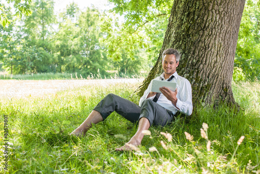 handsome grey hair man using a tablet, barefoot in the grass handsome grey hair man using a tablet, barefoot in the grass