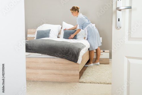 Young Maid Arranging Pillow On Bed