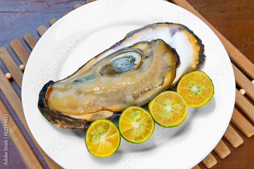 Opened fresh oyster in a white plate with lime on a wooden table