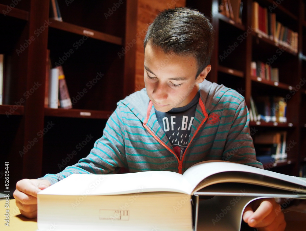 Teenager reading big book at library Teenager reading big book at library