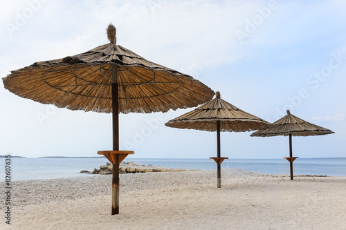 Strand mit Kies und Sonnenschirmen aus Schilf in Istrien