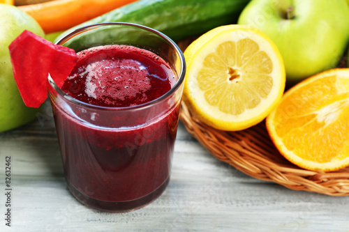 Glass of fresh juice, fruits and vegetables on wooden table, on bright background