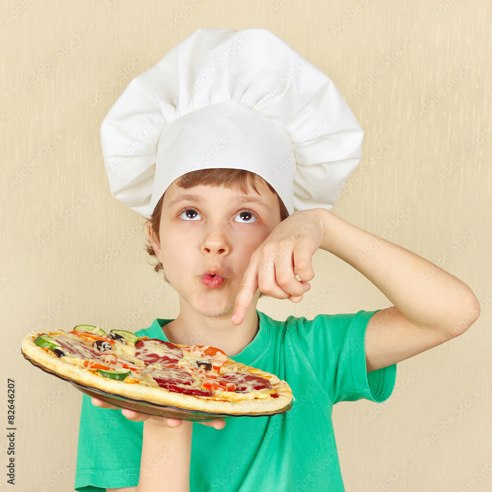 Young smiling kid in chefs hat with a cooked appetizing pizza Young smiling kid in chefs hat with a cooked appetizing pizza