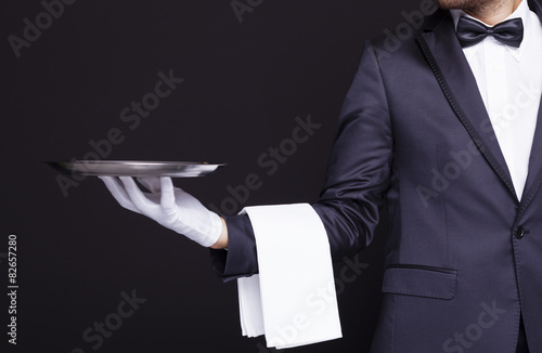 Waiter holding an empty silver tray against dark background