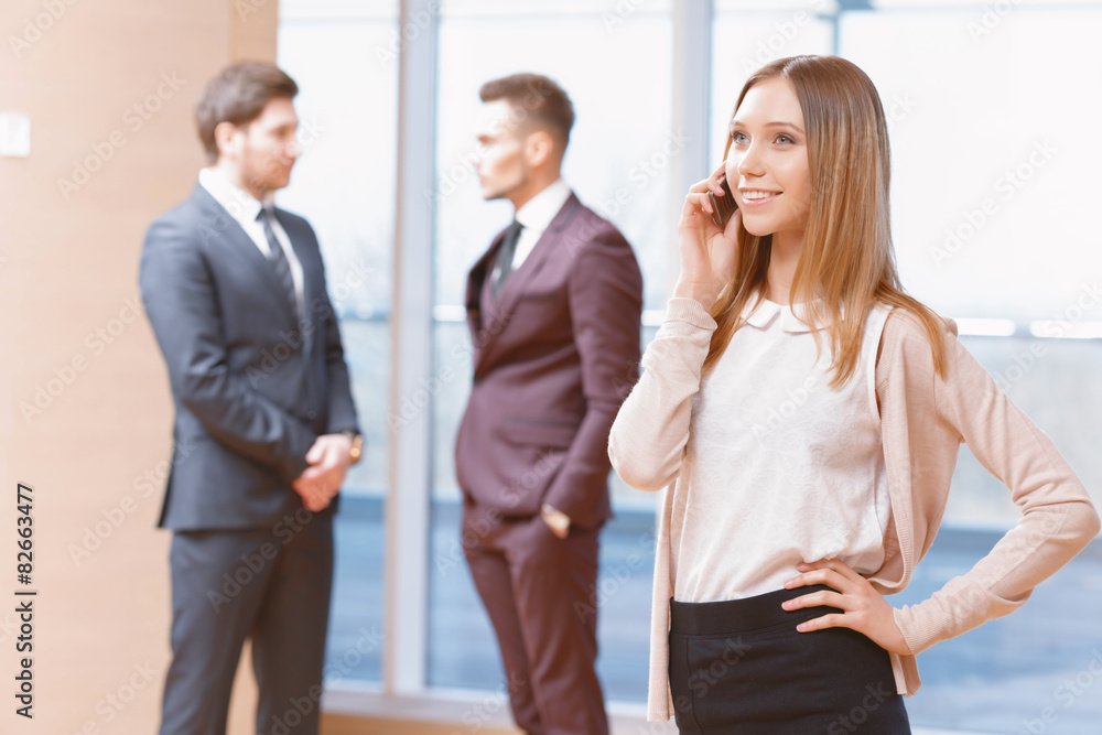 Blond young business woman standing in front of two men talking Blond young business woman standing in front of two men talking