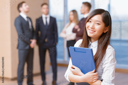 Asian young business woman standing in front of her co-workers 