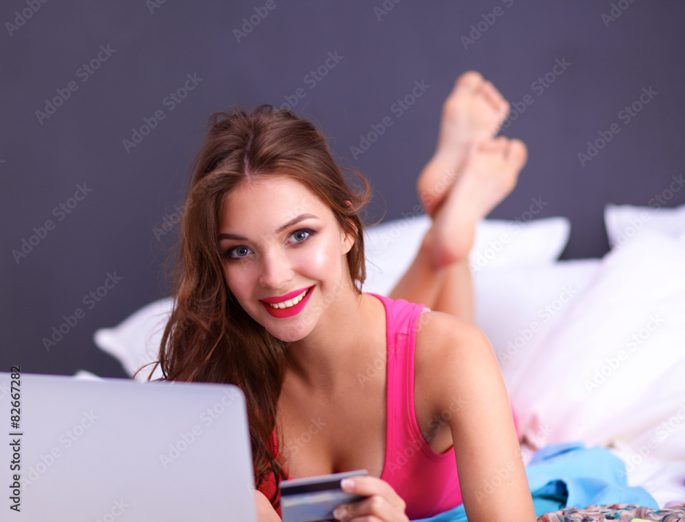 Beautiful woman lying on bed with a laptop and credit card Beautiful woman lying on bed with a laptop and credit card