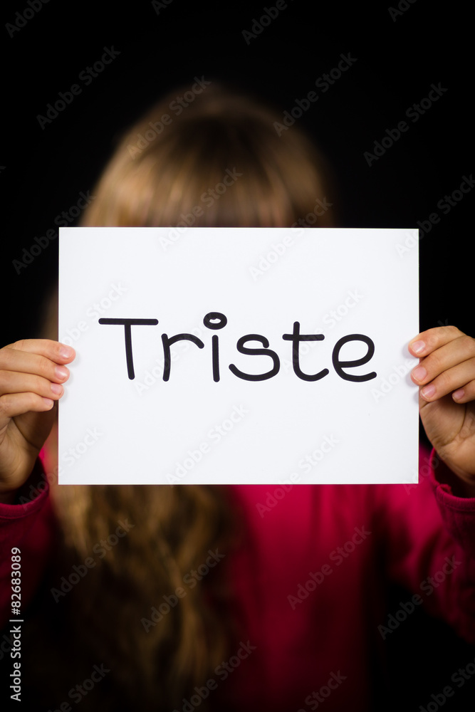 Child holding sign with Spanish word Triste - Sorry Child holding sign with Spanish word Triste - Sorry