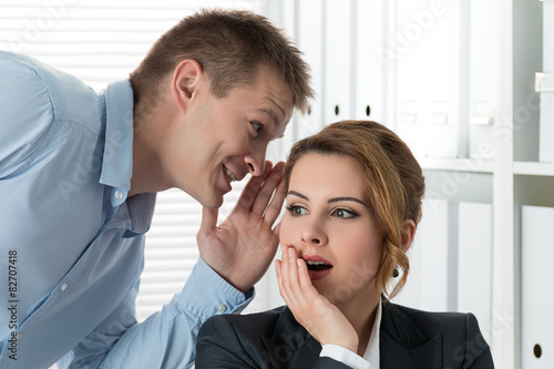 Quadro em tela Young man telling gossips to his woman colleague