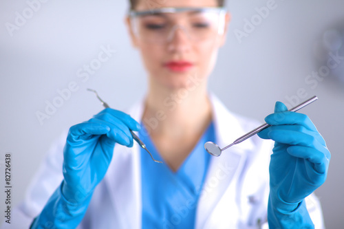 Attractive female dentist with tools , standing on gray