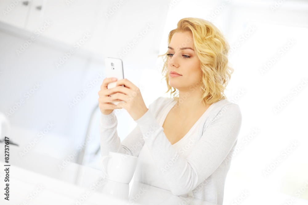 Young woman with smartphone in the kitchen Young woman with smartphone in the kitchen