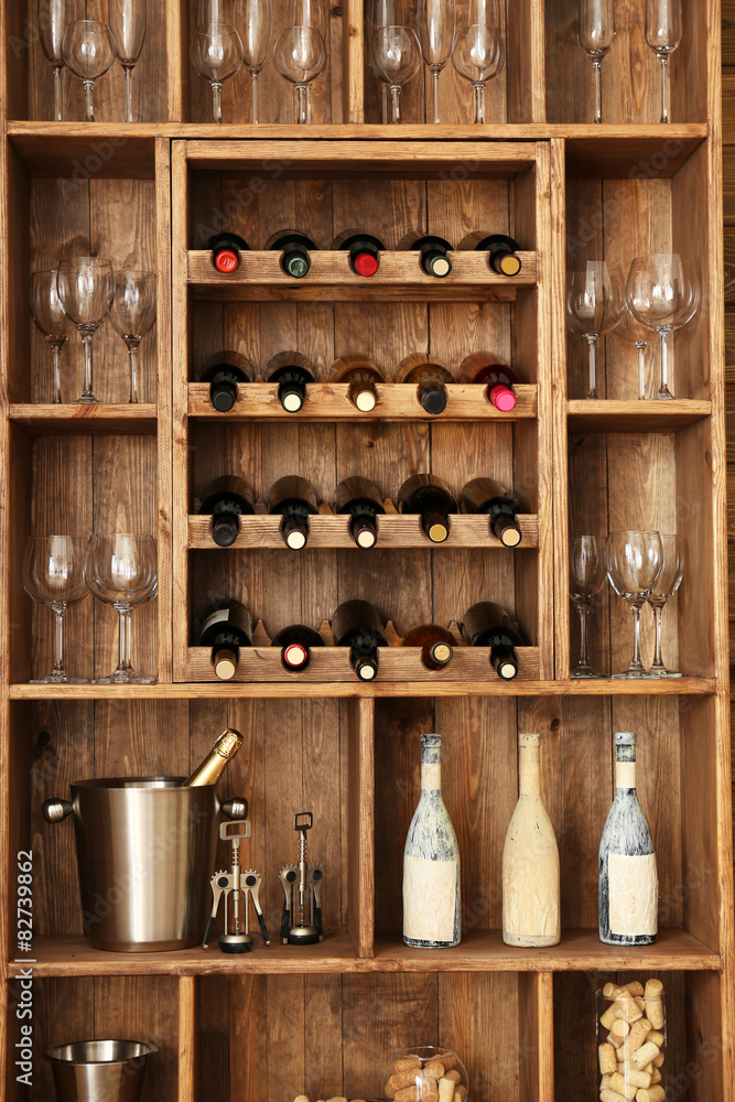 Shelving with wine bottles with glasses on wooden wall background
