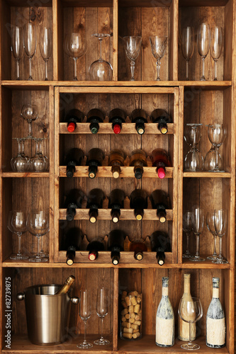 Shelving with wine bottles with glasses on wooden wall background