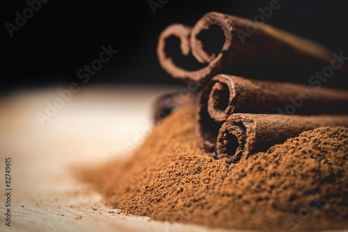 Fotografia Cinnamon sticks with cinnamon powder on wooden background