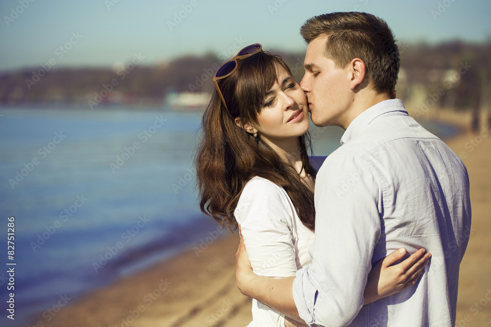 Cheerful couple embracing and posing on the beach on a sunny day Cheerful couple embracing and posing on the beach on a sunny day