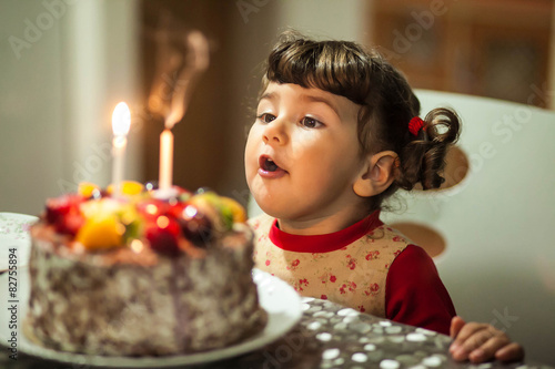 little girl blows out the 2 candles on the cake in her birthday