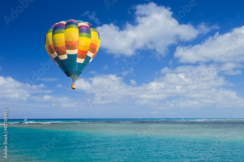Hot air balloon over ocean and clouds blue sky