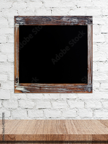 Blank vintage chalk board over table on white brick wall