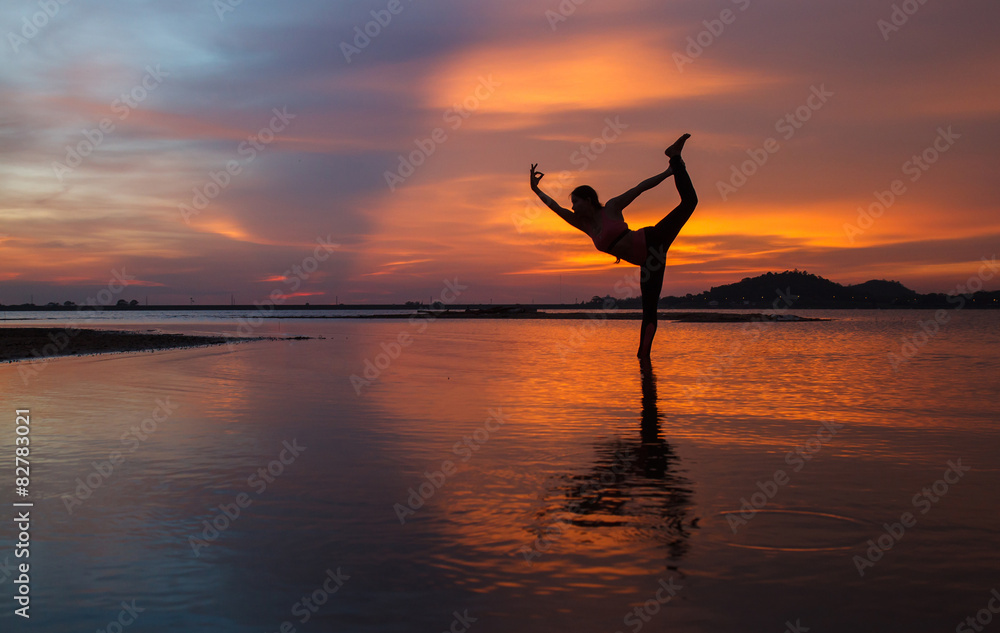 Silhouette of young woman practicing yoga on the lake at sunset