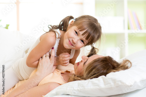 Mother and her child play and laugh in bed enjoying  sunny