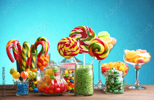Colorful candies in jars on table on blue background