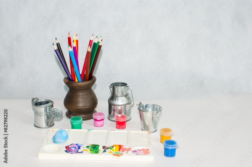 colored pencils in a ceramic vase, a palette and paints on a lig colored pencils in a ceramic vase, a palette and paints on a lig