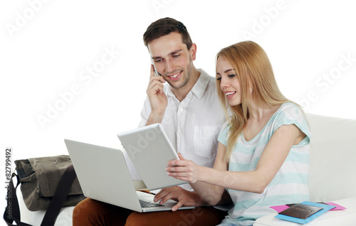 Portrait of young happy couple with baggage, digital tablet and laptop sitting on sofa. Isolated on white