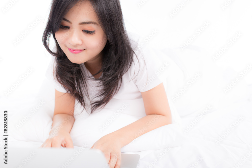 Smiling woman using a laptop while lying on her bed Smiling woman using a laptop while lying on her bed