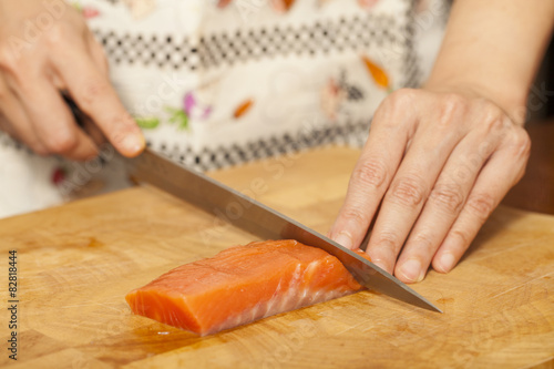 an Asian woman chef preparing salmon piece with sharp knife