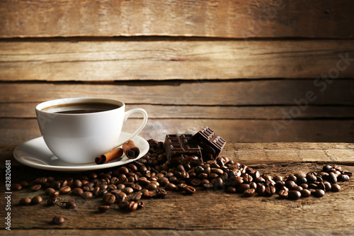 Cup of coffee with grains, chocolate and cinnamon sticks on wooden background