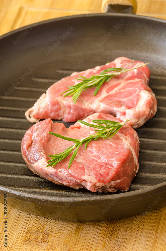 Raw steak with rosemary on cast-iron frying pan