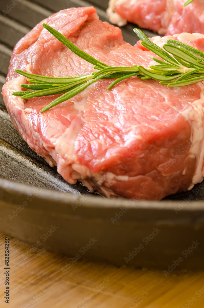 Raw steak with rosemary on cast-iron frying pan