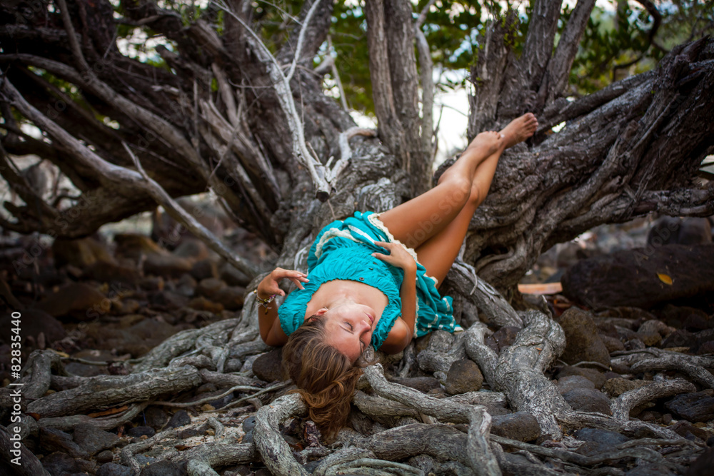 Beautiful young woman in a turquoise dress lying on roots of