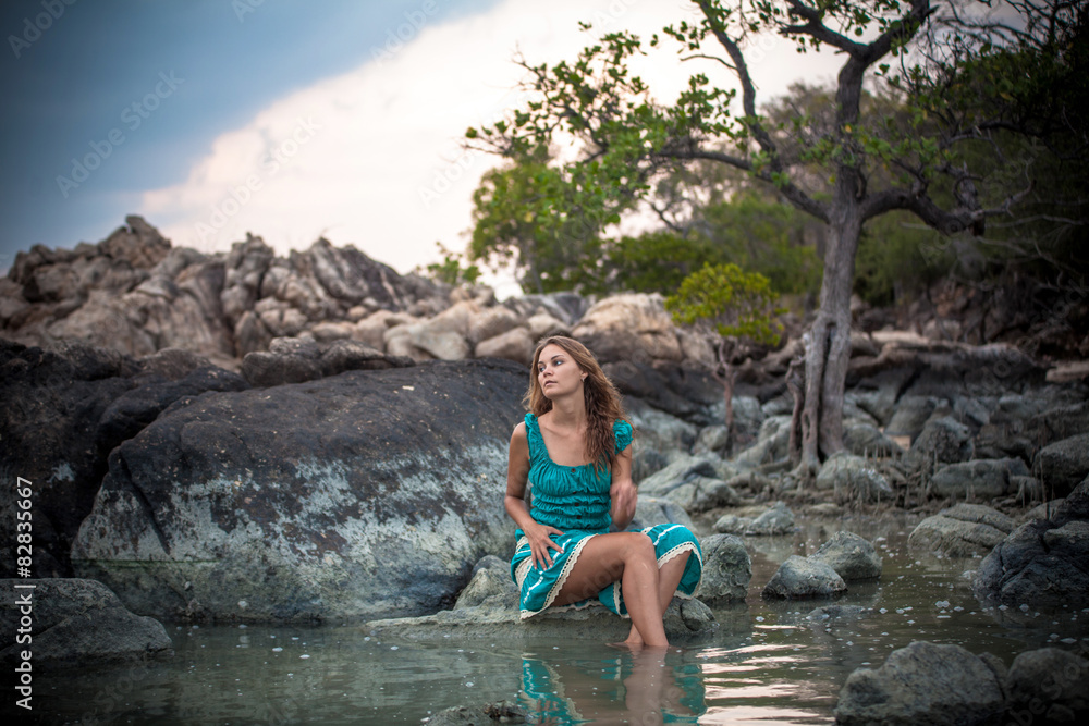 Young beautiful woman in long turquoise dress sitting on a stone Young beautiful woman in long turquoise dress sitting on a stone