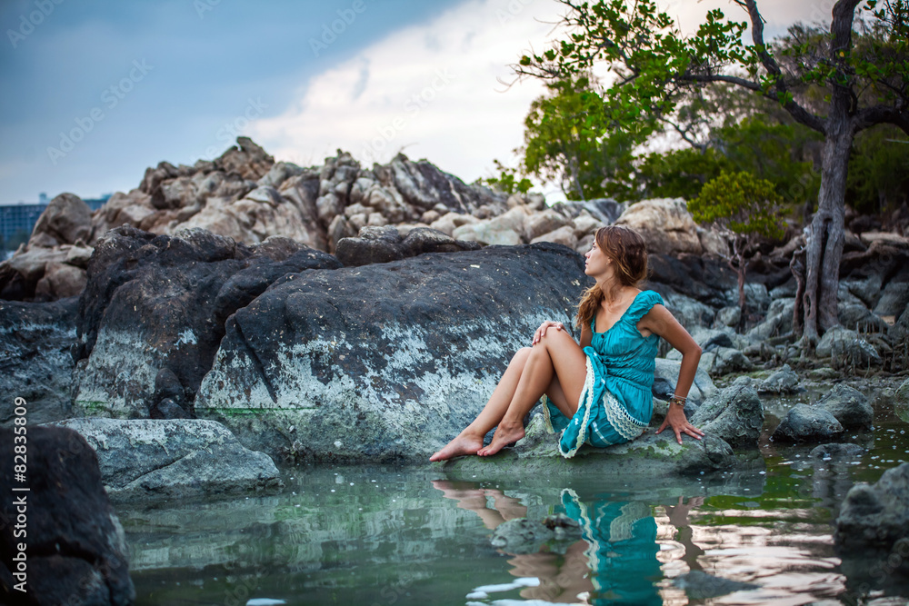 Young beautiful woman in long turquoise dress sitting on a stone Young beautiful woman in long turquoise dress sitting on a stone