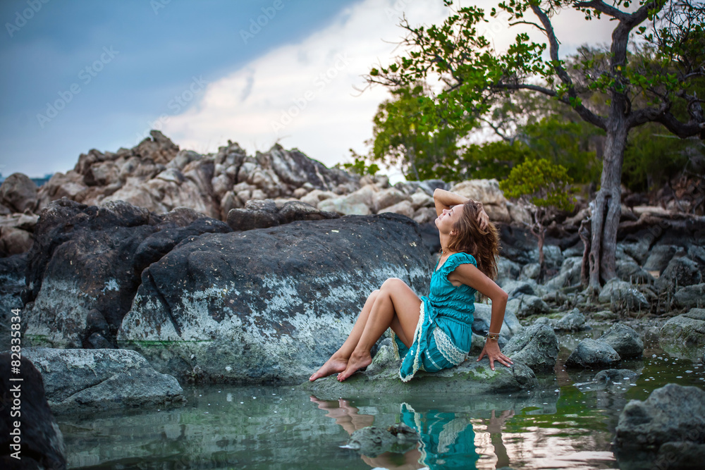 Young beautiful woman in long turquoise dress sitting on a stone Young beautiful woman in long turquoise dress sitting on a stone