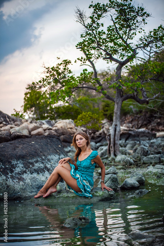 Young beautiful woman in long turquoise dress sitting on a stone © emaria